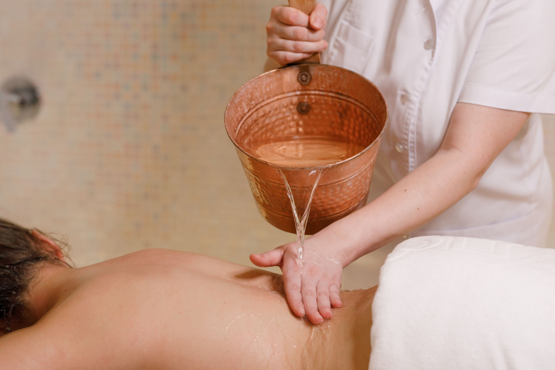 Therapist rinsing a guest with warm water from a copper hammam bowl
